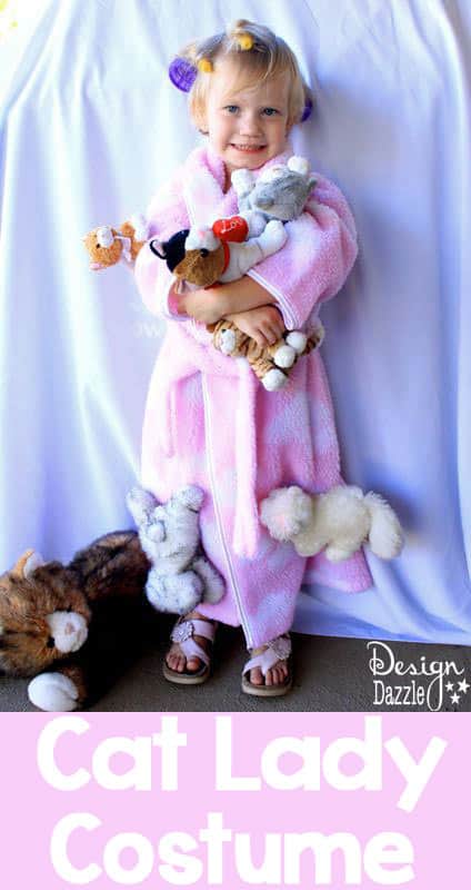 little girl dressed like a cat lady in a robe and wig with stuffed cats