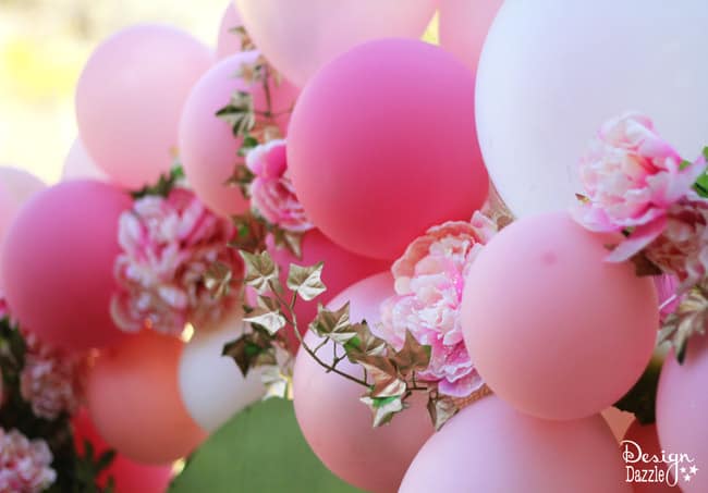 Balloons And Flowers Make a Beautiful Fairy Arch. Tutorial on how to use balloons and dollar store flowers to create this beautiful show stopper party decor on a budget! Design Dazzle #fairyparty #DIYfairyparty #balloonflowerarch