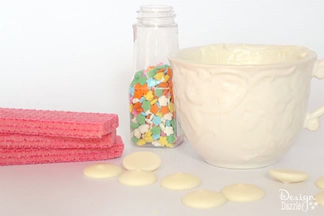 All that is needed to make fairy cookies are strawberry wafers, white candy melts, and rainbow sprinkles. Easy sweet treat! See more on design dazzle.com #fairycookies #diyfairyparty