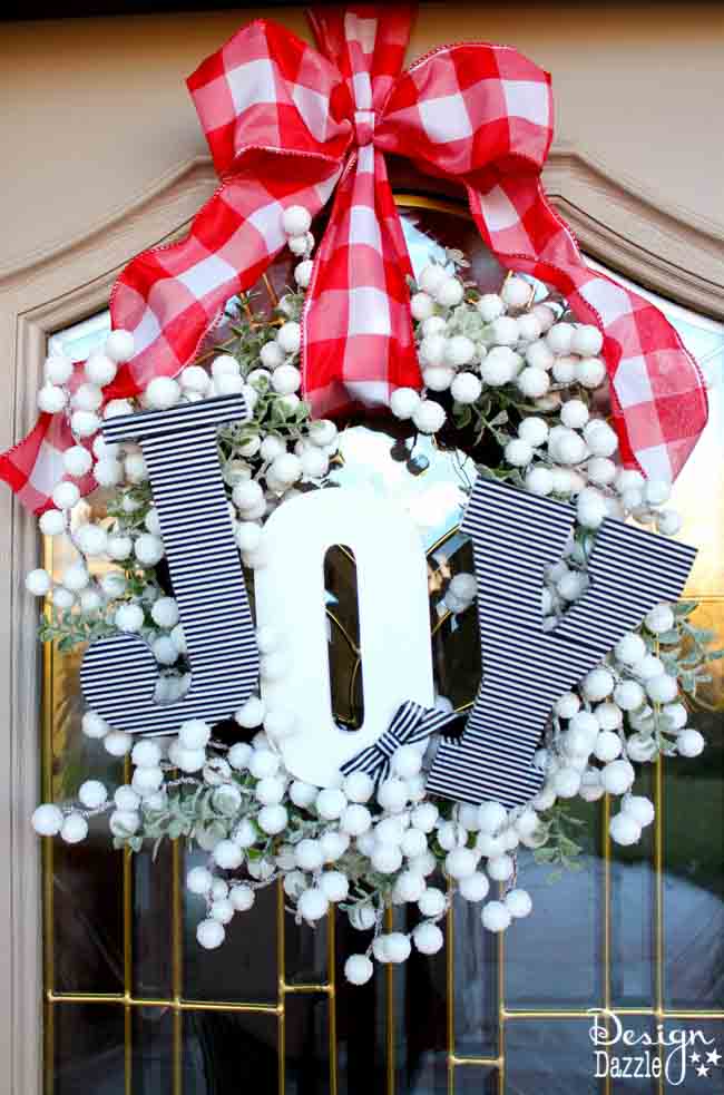 A wreath of white snowberries and greenery with black and white striped wooden letters spelling JOY and a red gingham bow