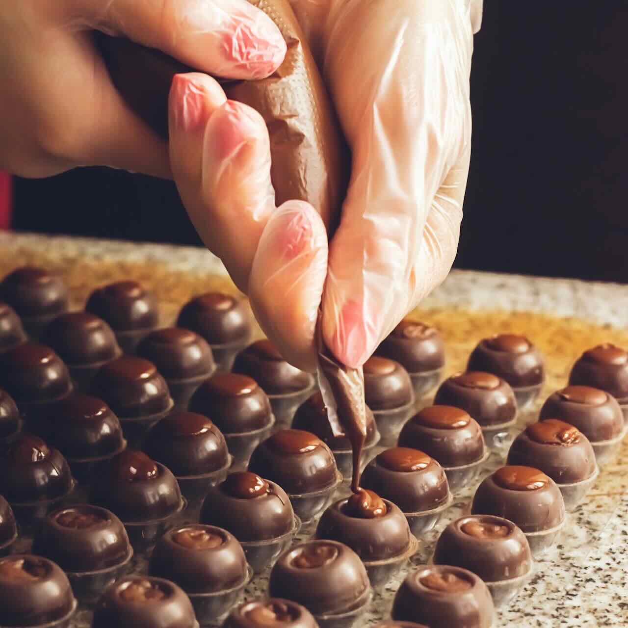Making handmade chocolates A confectioner pours liquid dark chocolate into molds Close up Selective focus Square
